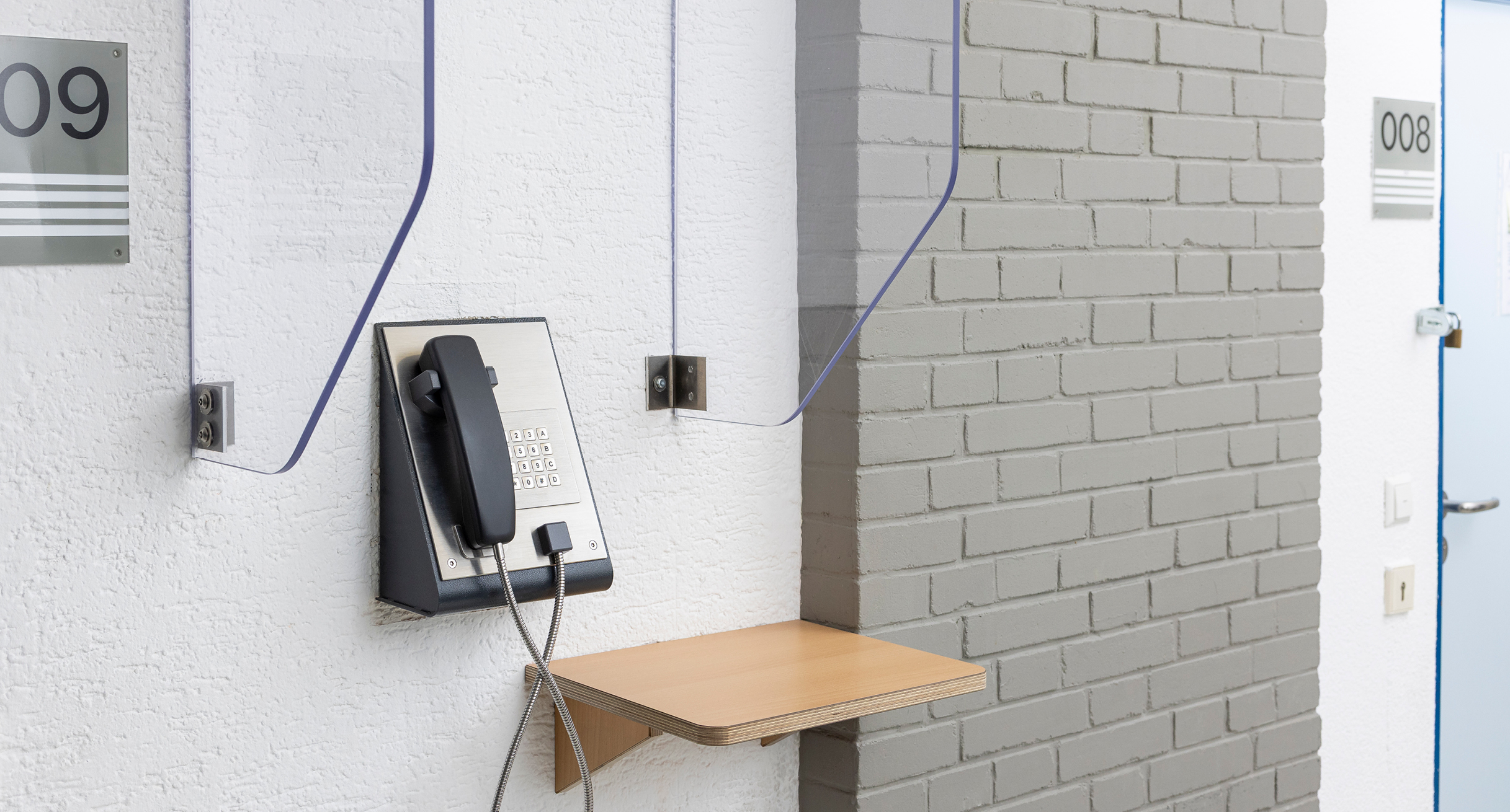 Ein Telefon hängt an der Wand, dahinter ist ein Gang innerhalb einer Justizvollzugsanstalt zu sehen.